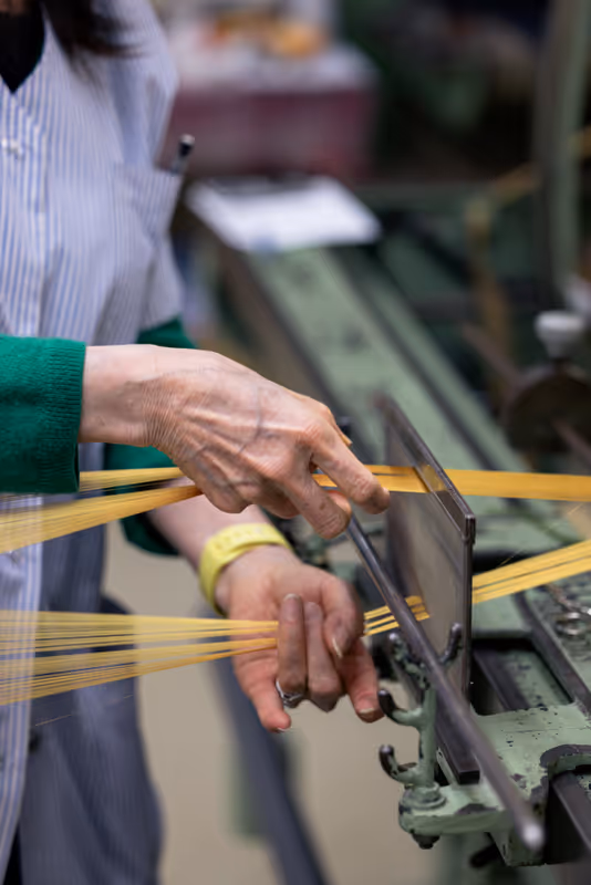 Hands guiding golden silk threads through a weaving machine
